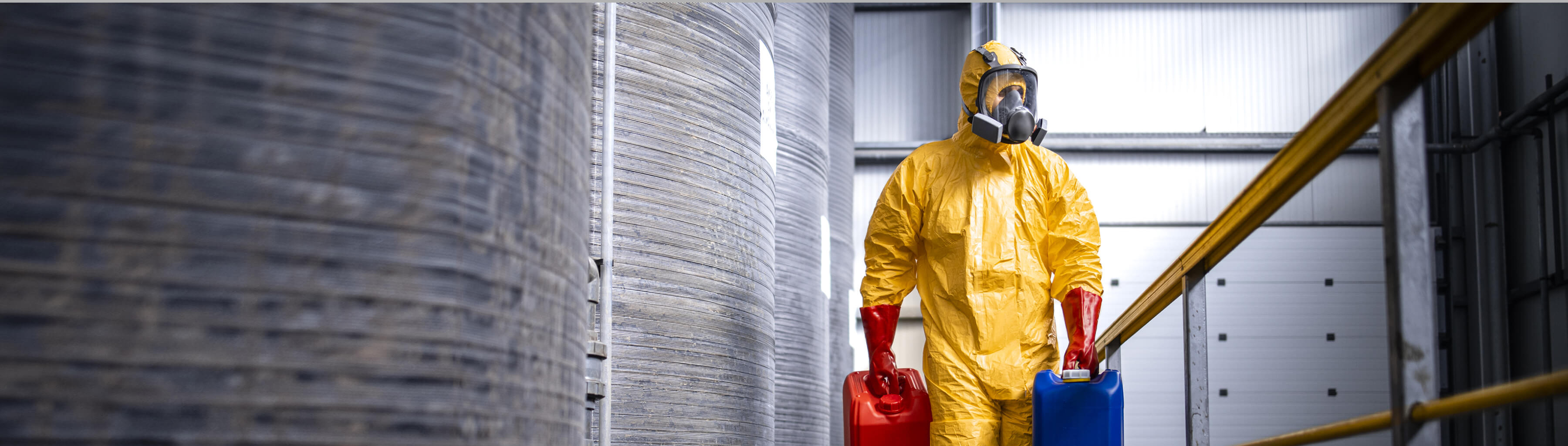 Factory worker in protective equipment walking by acid storage tanks and carrying aggressive and dangerous chemicals.