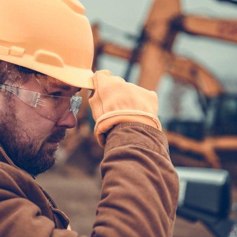 Closeup of Professional Construction Worker Wearing Yellow Hard Hat, Protective Glasses and Gloves. Industrial Safety Equipment Theme.