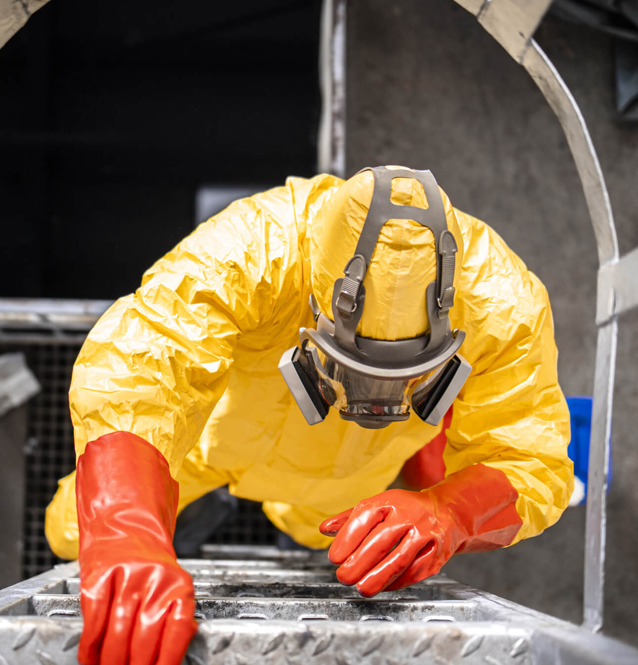 Top view of worker in protective suit and gas mask climbing metal industrial ladder inside chemicals factory