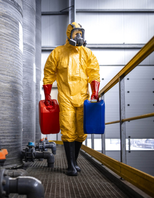 Factory worker in protective equipment walking by acid storage tanks and carrying aggressive and dangerous chemicals. Factory worker in protective equipment walking by acid storage tanks and carrying aggressive and dangerous chemicals.