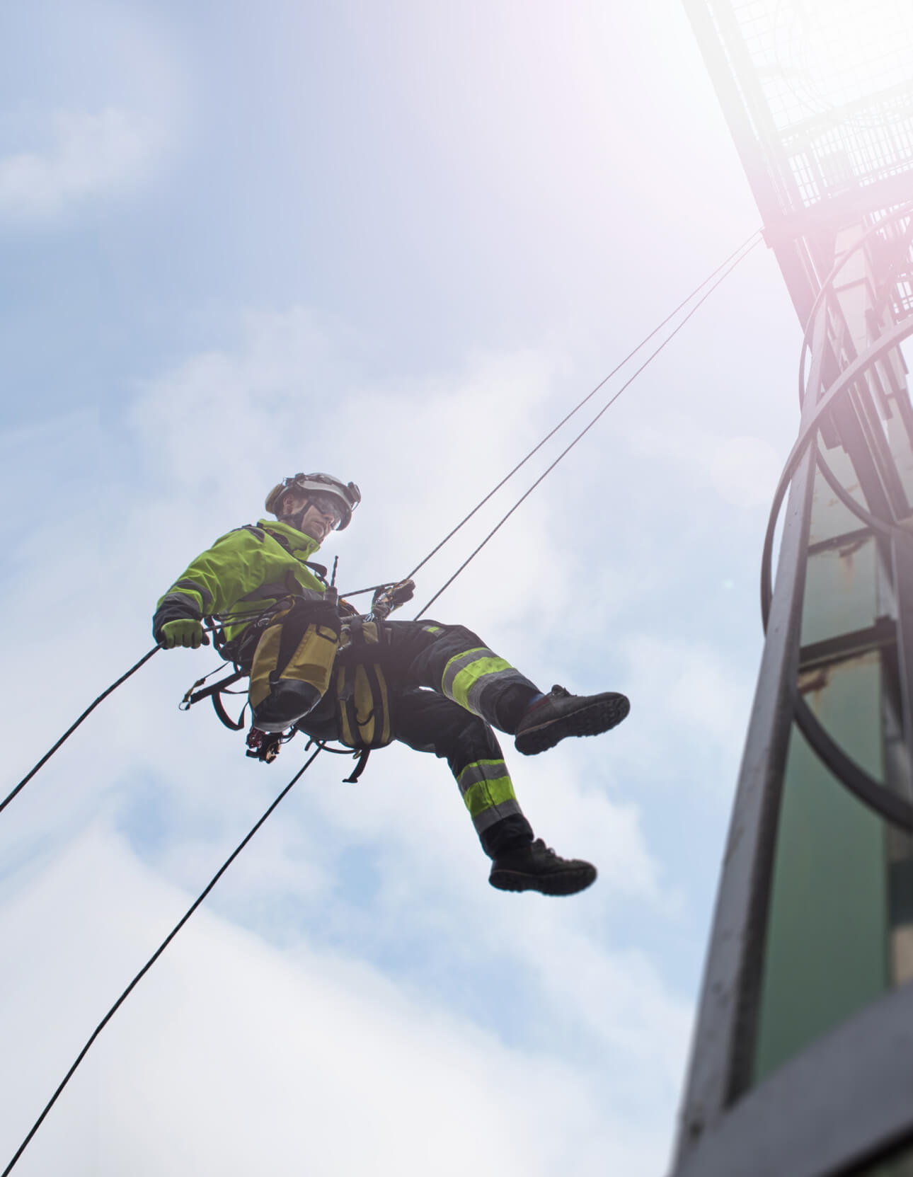 Manual rope access technician - worker abseil from tower - antenna in sun Manual rope access technician - worker abseil from tower - antenna in sun